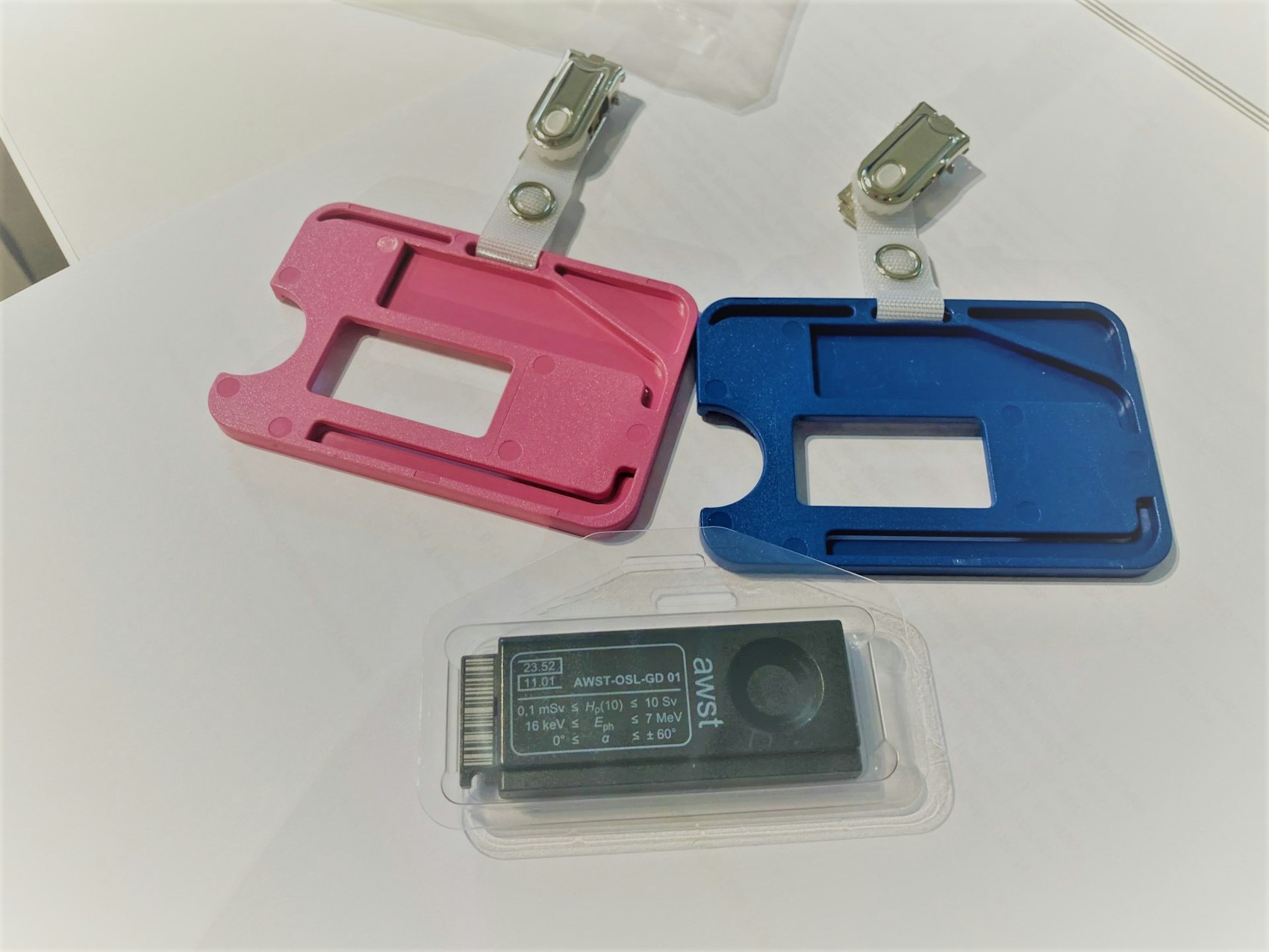 Ein OSL-Dosimeter liegt zusammen mit einem blaen und rosafarbenen Trägerrahmen auf einem Tisch