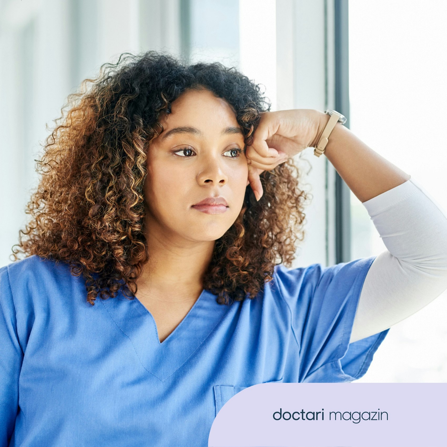 Junge Ärztin blickt nachdenklich aus dem Fenster.
