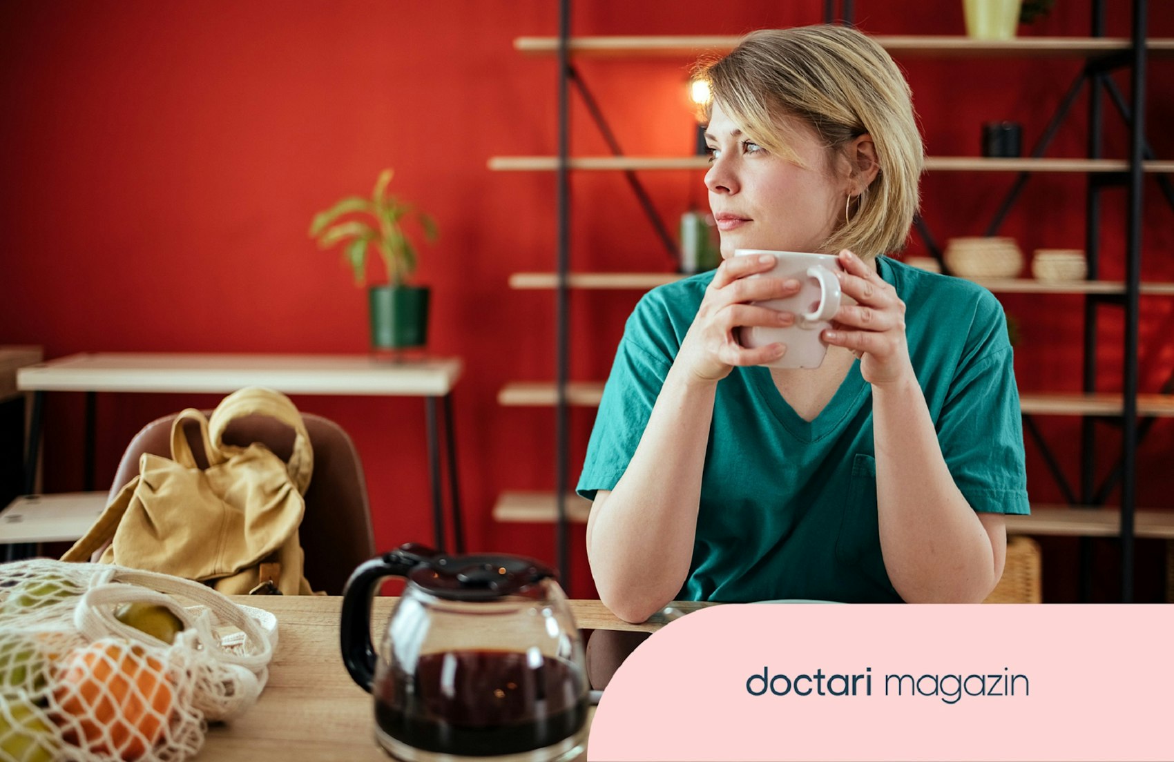 Junge, medizinische Fachkraft sitzt am Frühstückstisch und hält einen Kaffee in der Hand.