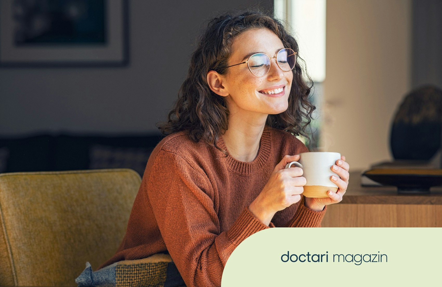 Junge Frau sitzt auf einem Sofa und hält eine Tasse in der Hand.