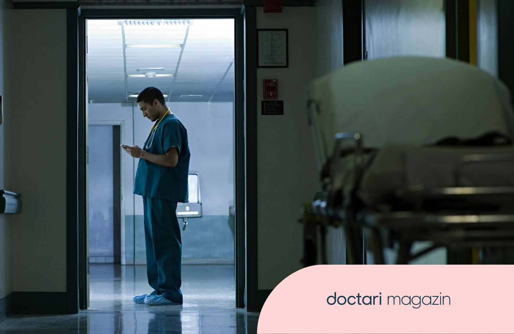 Ein Krankenpfleger steht nachts auf einem Krankenhausflur und schaut auf sein Handy.
