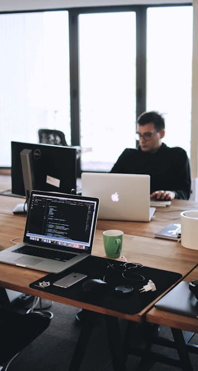 Schreibtisch mit Macbooks und einer arbeitenden Person