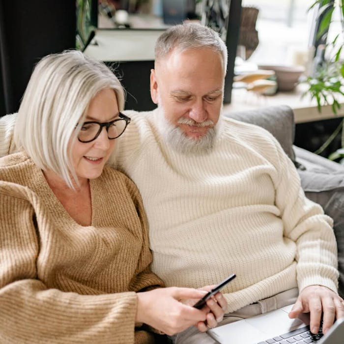 Ein älteres Paar sitzt mit einem Laptop auf dem Schoß auf dem Sofa