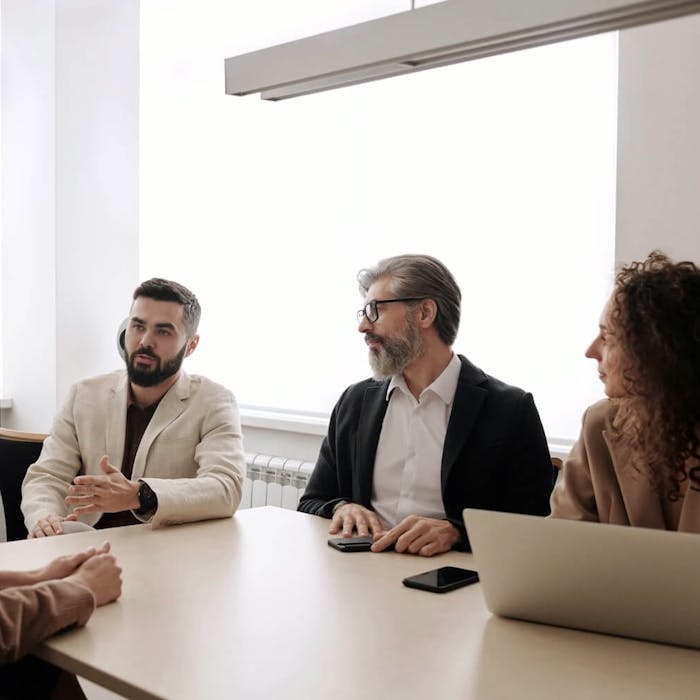 Vier Personen sitzen an einem Besprechungstisch mit einem Laptop auf dem Tisch