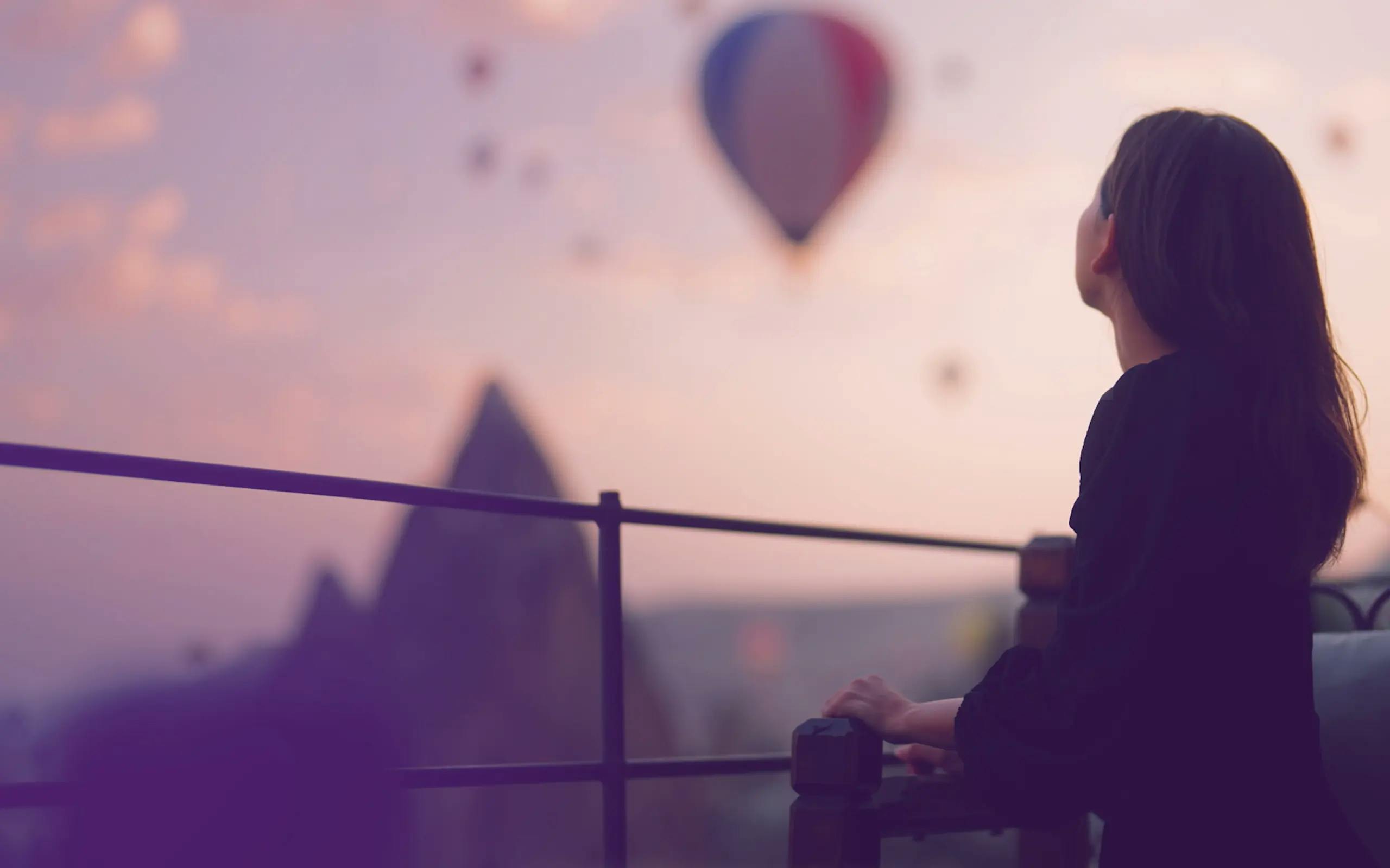 Woman on balcony looking out at lots of hot air balloons