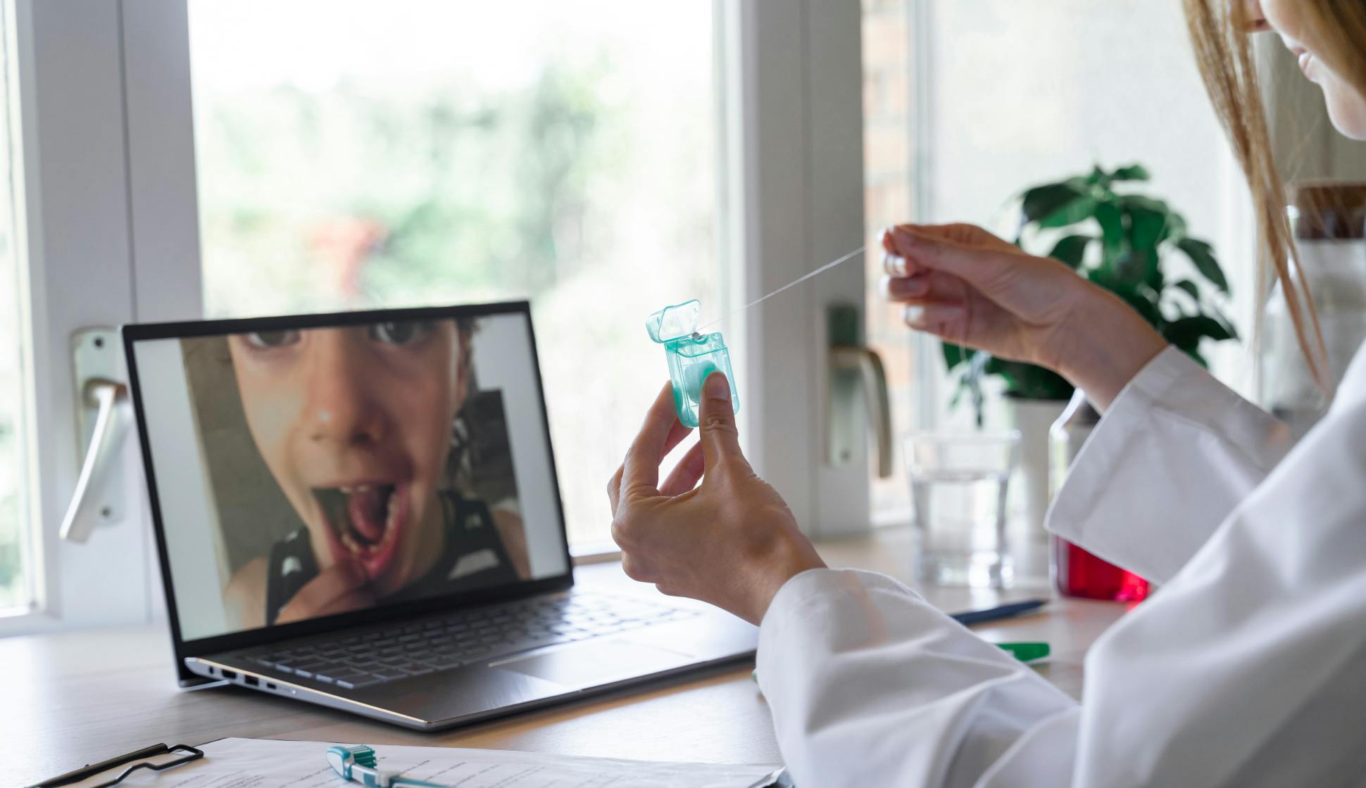 Dentist explaining some procedure to her young patient through a telemedicine call on a laptop