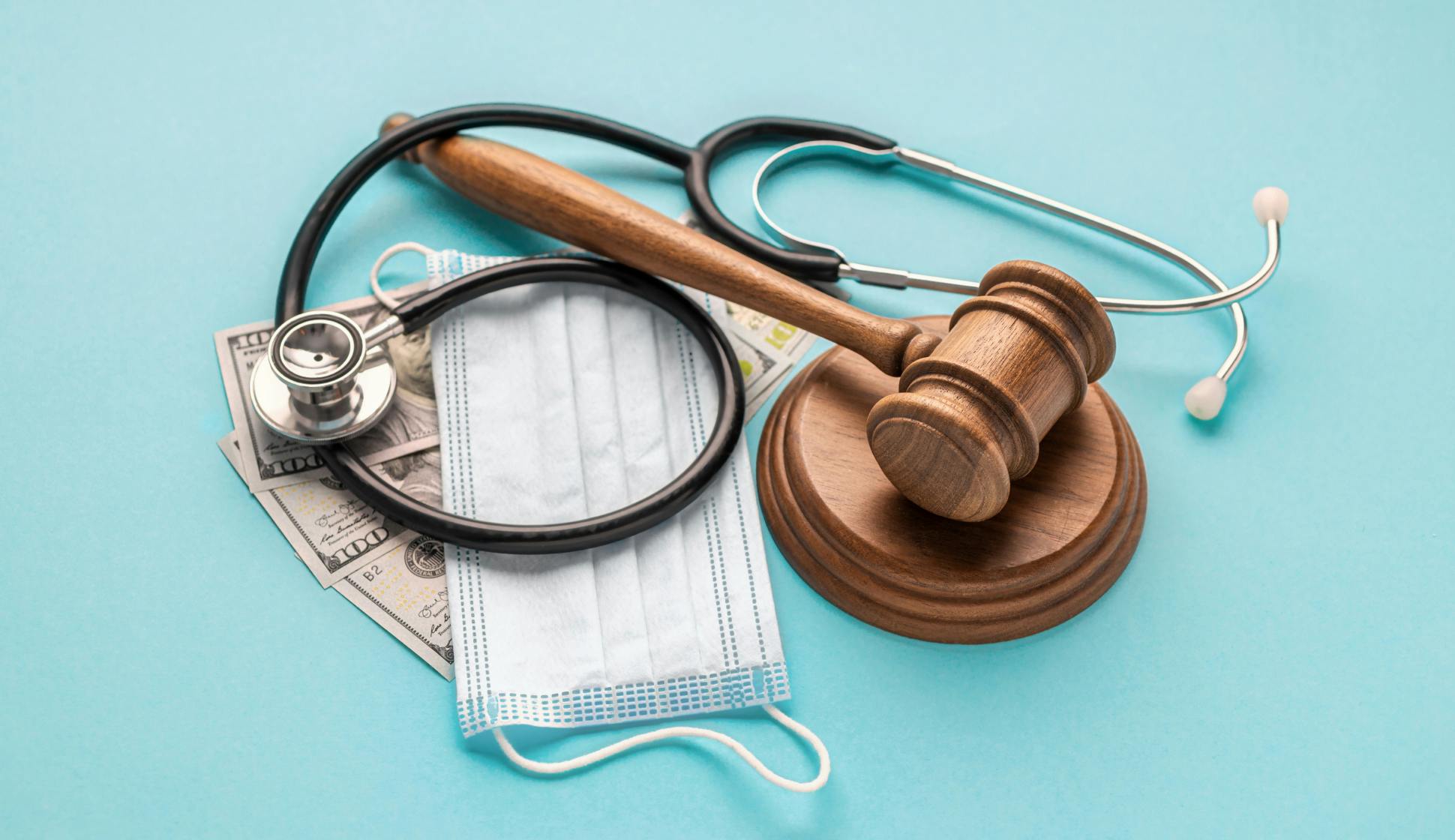 A medical mask, a stethoskop, cash and judge hammer lying on a table