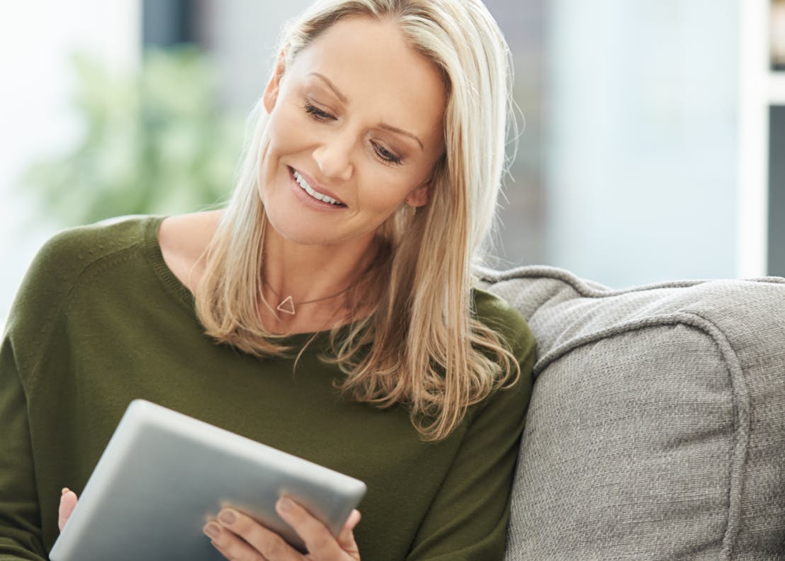 Person sitting on a couch, smiling while using a tablet.