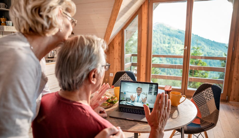 Older couple waiving to their doctor during a telemedicine call on their laptop