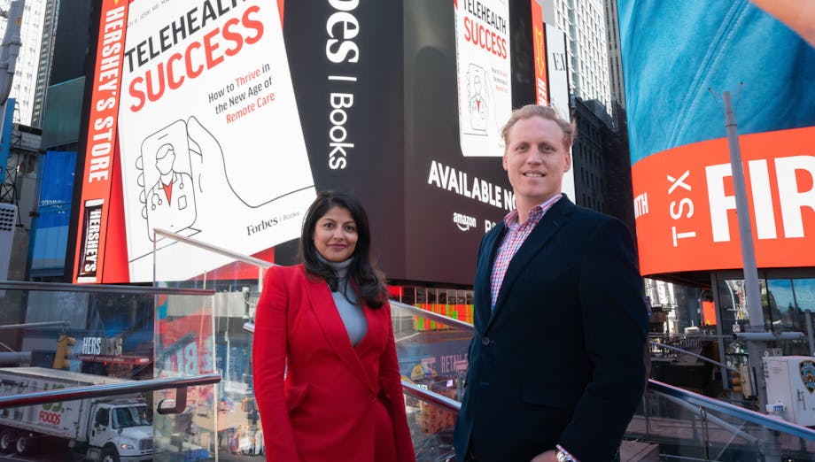 Drs. Welch and Joshi in Times Square, with an image of their book in the background