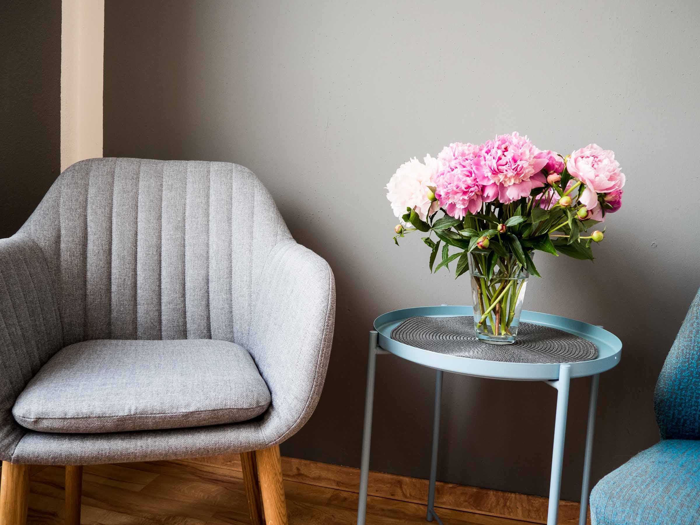 Ein grauer Sessel neben einem kleinen Runden Tisch, auf dem ein Blumenstrauß steht