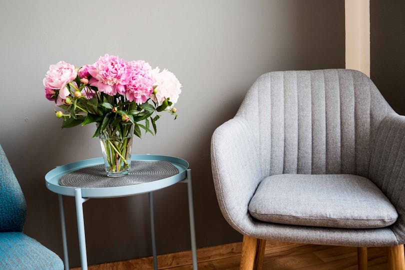 Atmosphärisches Bild eines Sessels in einem Wartezimmer mit einem mit Blumen geschmückten, kleinen Tisch daneben