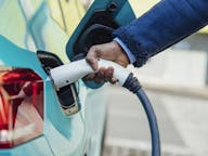 Close up of someone plugging in a light blue electric car to charge