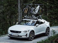 Polestar 2 with bike rack on roof driving through forrest 
