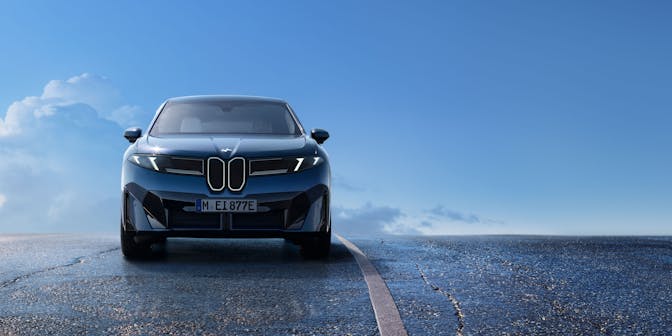 BMW Ix3 electric car with updated styling driving on a open road with clouds in the background