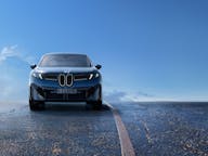 BMW Ix3 electric car with updated styling driving on a open road with clouds in the background