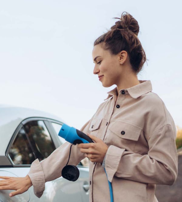 girl plugging in electric car to charge, holding a blue charging cable