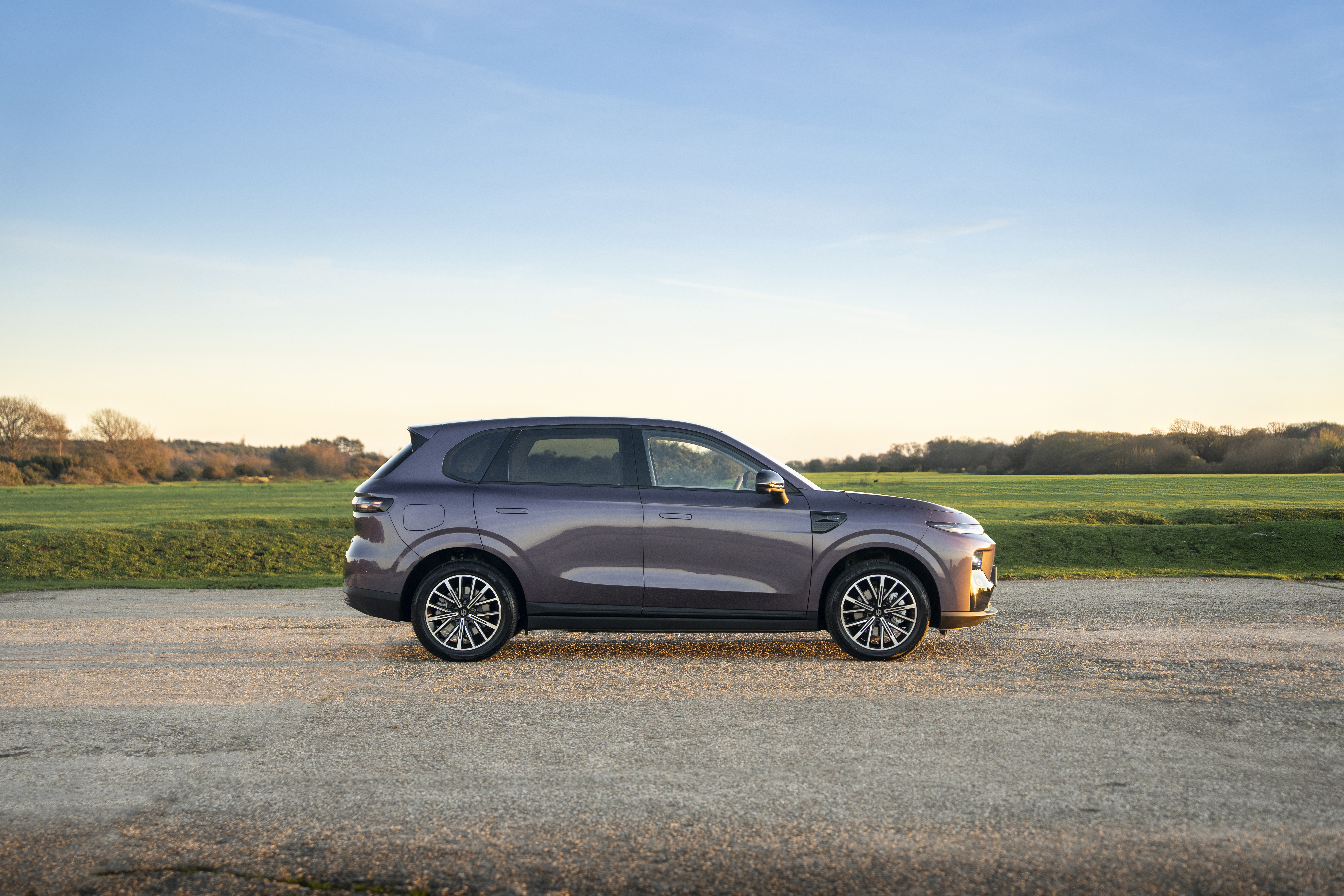 Leapmotor electric car side view, in car park with green field behind