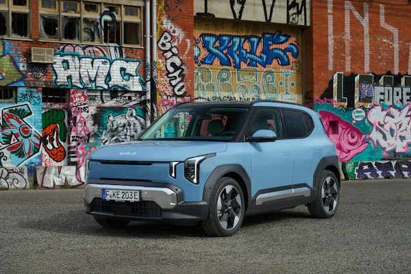 Kia EV 2 electric car in blue parked in front of graffiti wall 