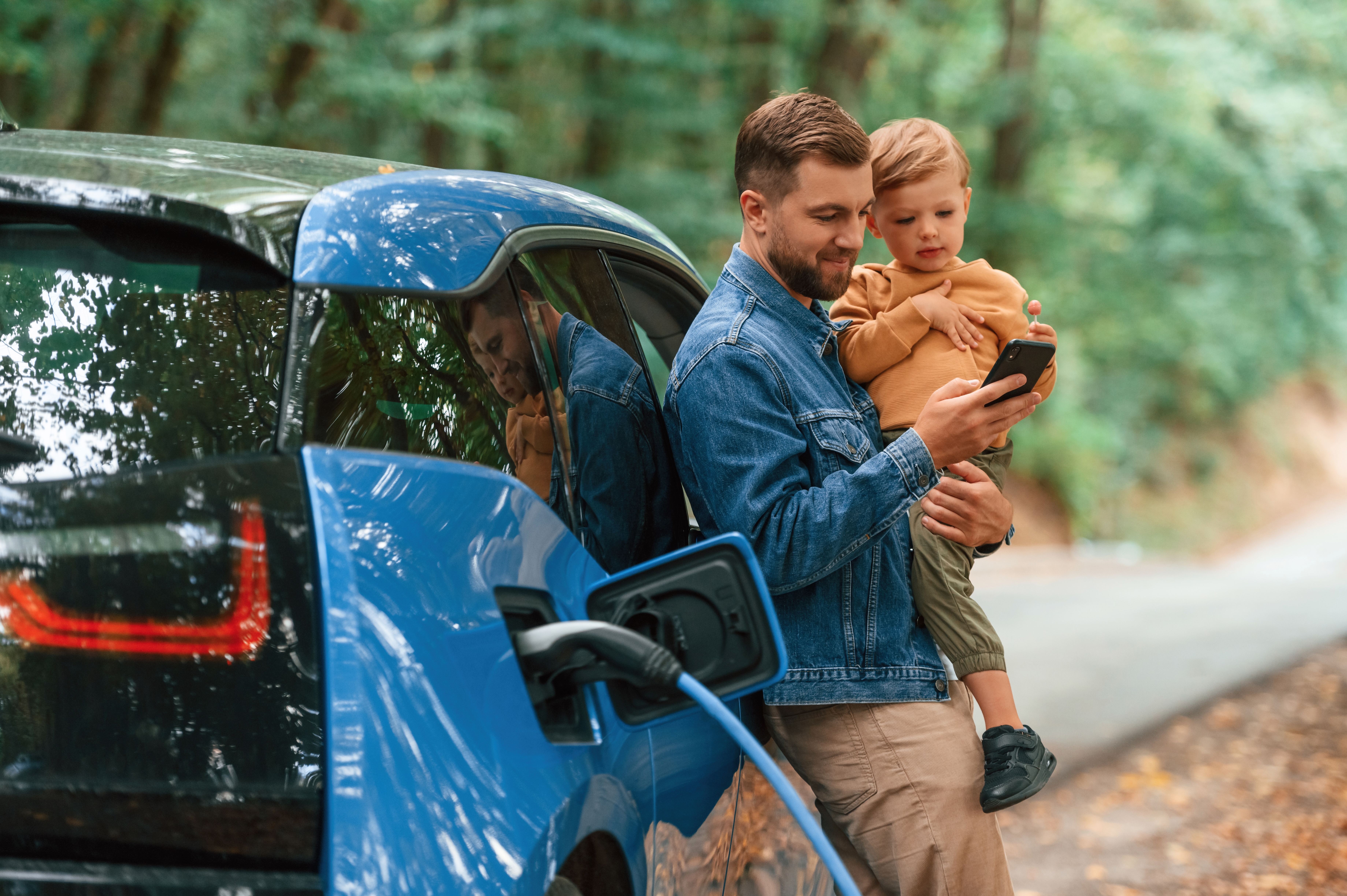 father and son standing next to electric car