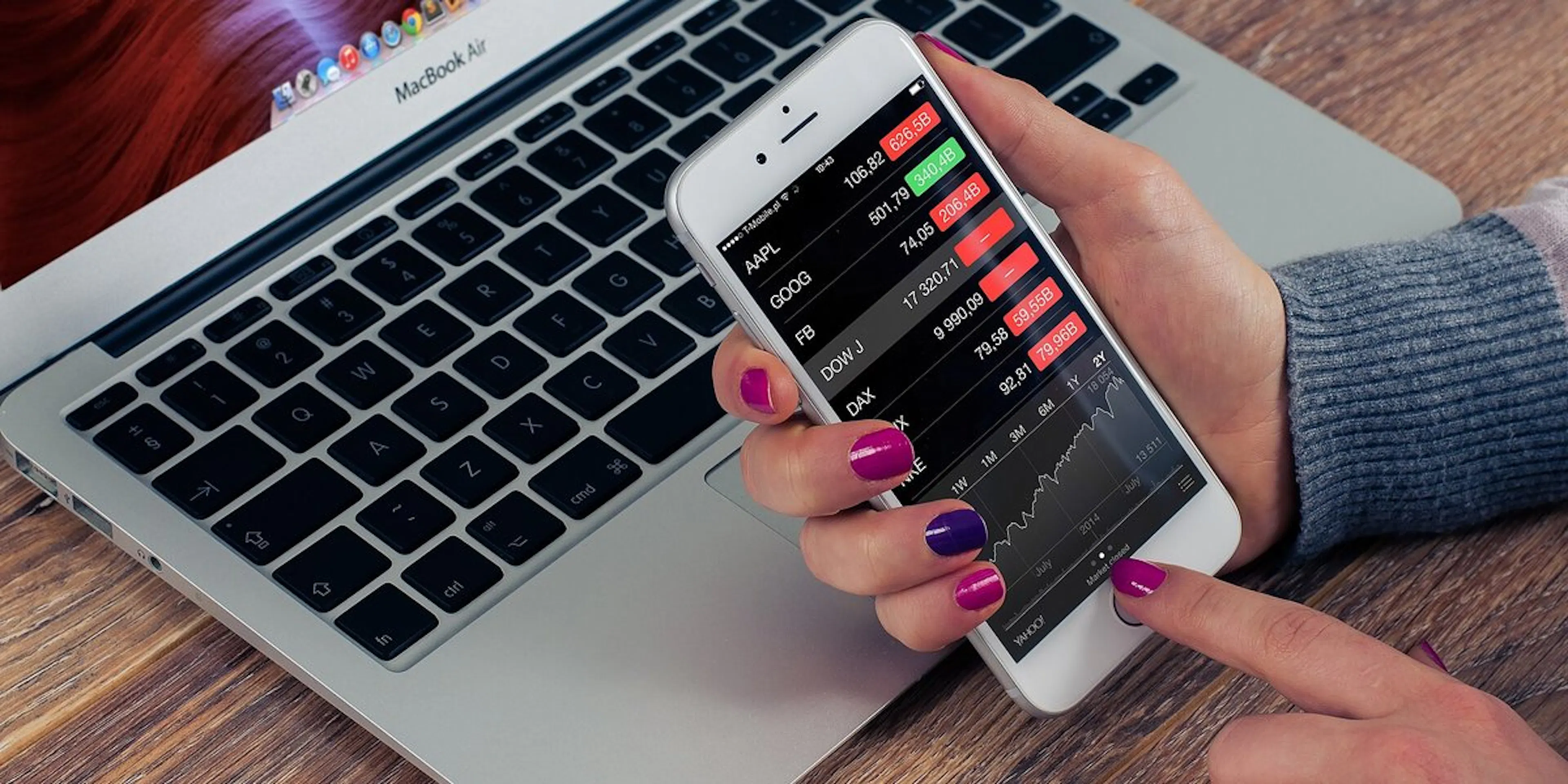 Checking stock prices on a phone beside a laptop