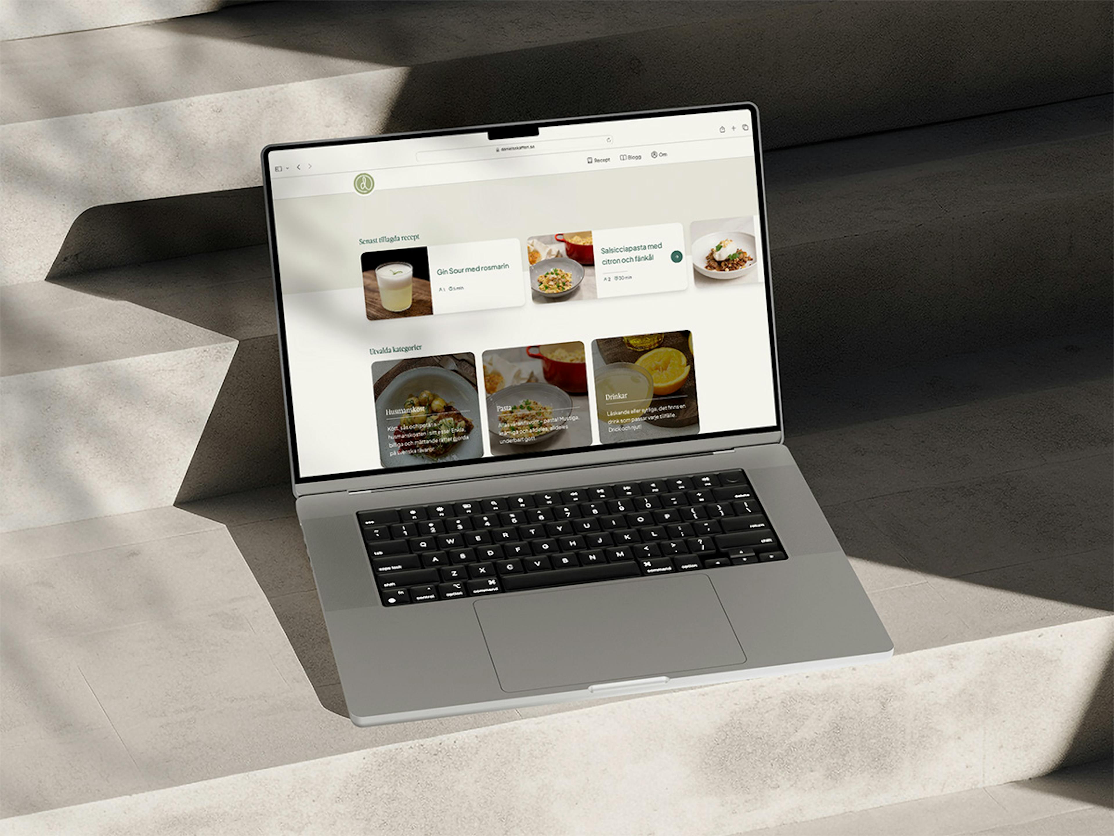 An MacBook Pro sitting on a concrete stairway displaying the recipe website