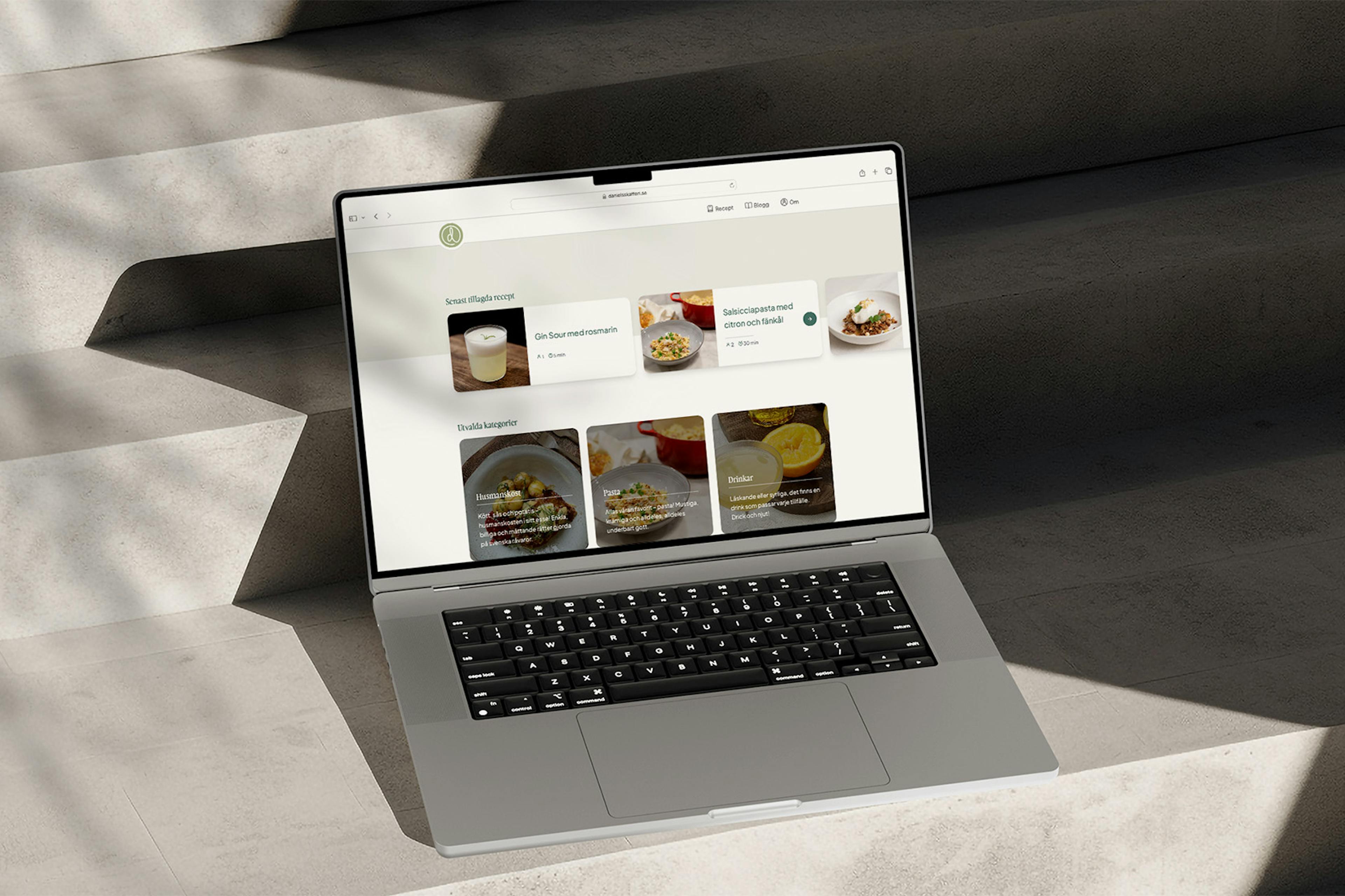 An MacBook Pro sitting on a concrete stairway displaying the recipe website