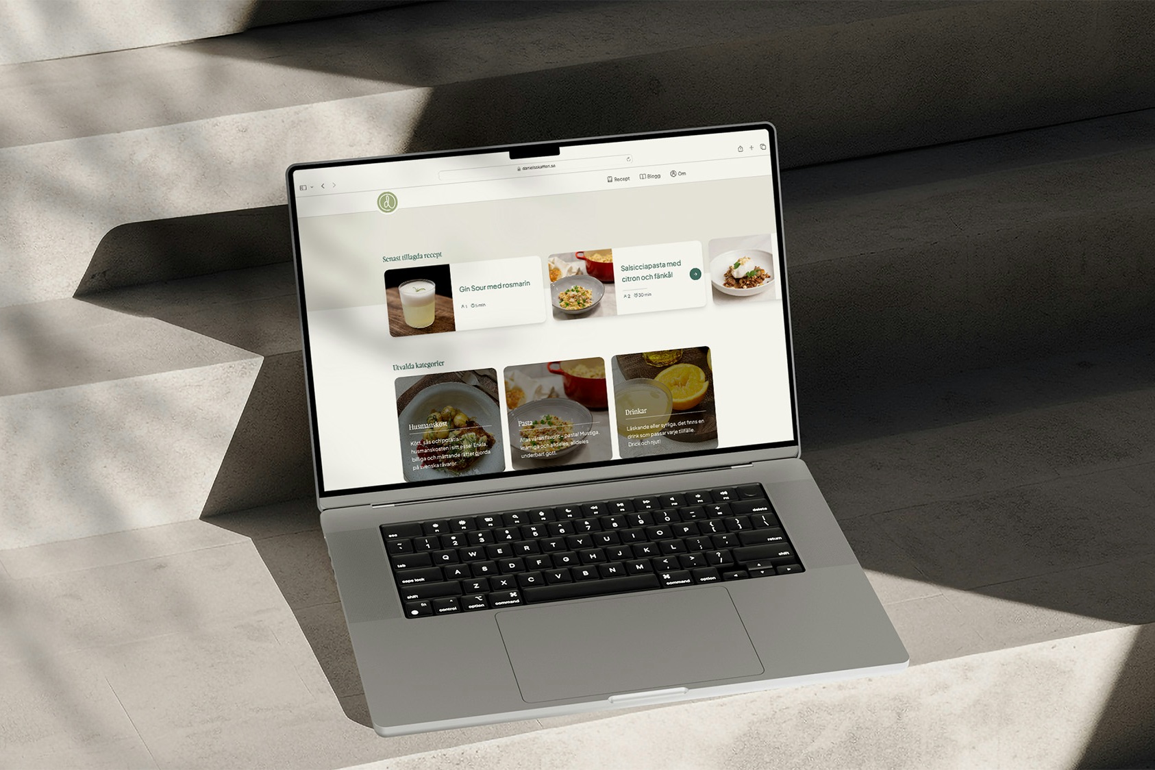 An MacBook Pro sitting on a concrete stairway displaying the recipe website