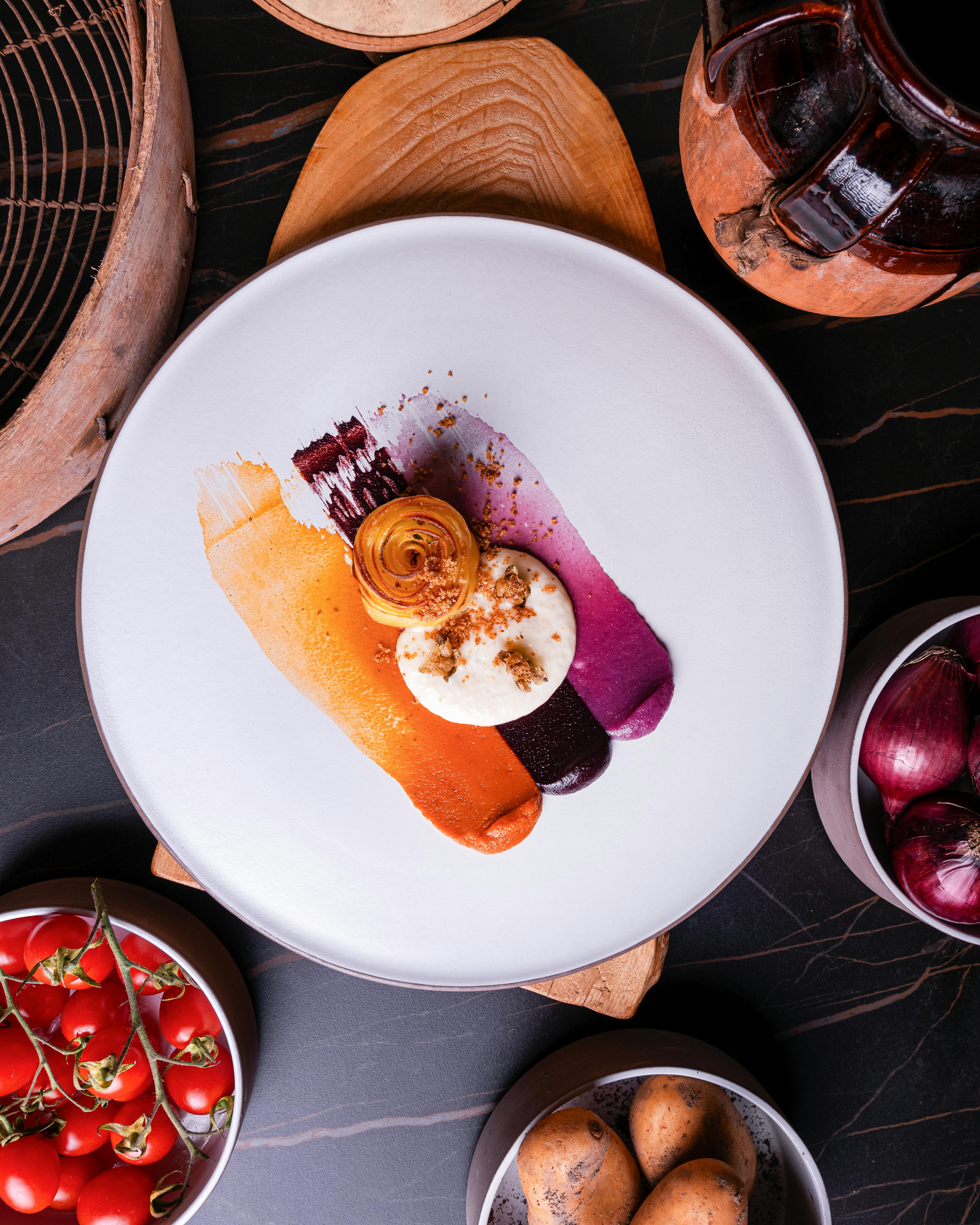 Millefoglie di patate su creme di pomodorini datterini arrostiti, cipolla rossa in agrodolce e olive Celline, spuma di pecorino, capperi fritti, crumble di pane alle acciughe ed essenze di macchia mediterranea 