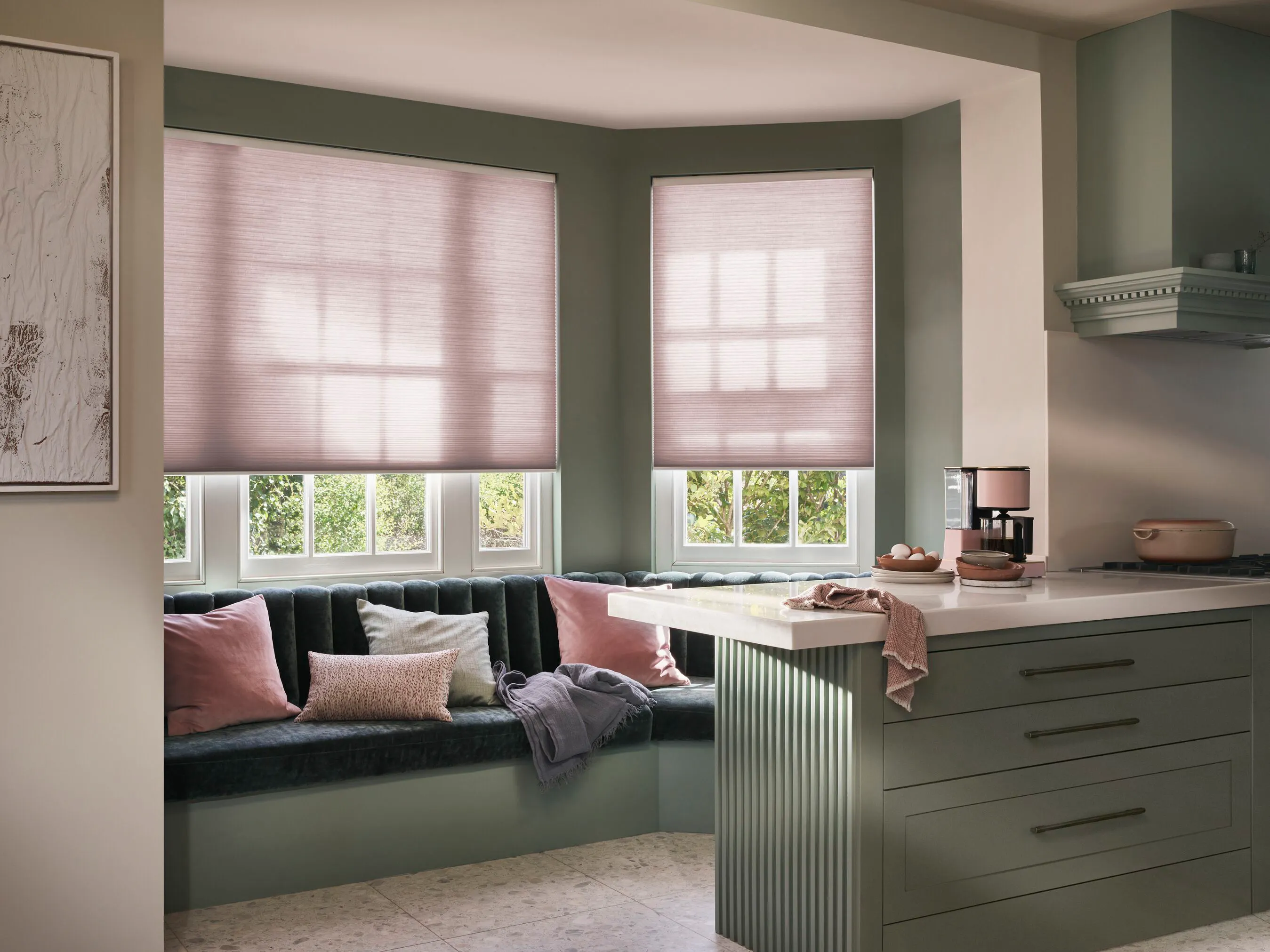 Soft pink Duette® honeycomb blinds on a bay window in a cosy light kitchen