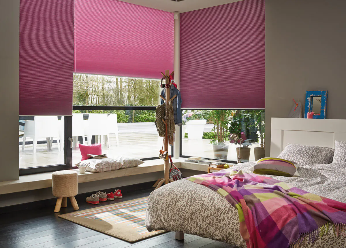 Pink Duette® blinds on large windows in a vibrant bedroom