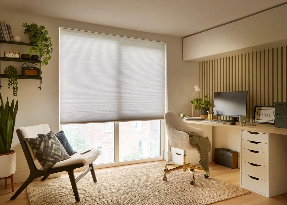 Light grey half-closed Duette® honeycomb blinds on a large windows in a light home office 