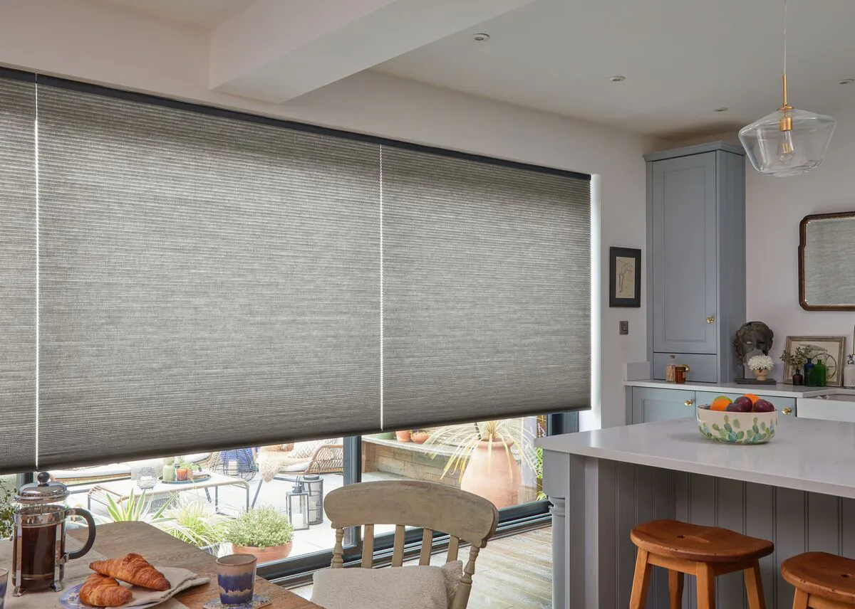Grey half-closed Duette® honeycomb blinds on a large windows in a cosy kitchen