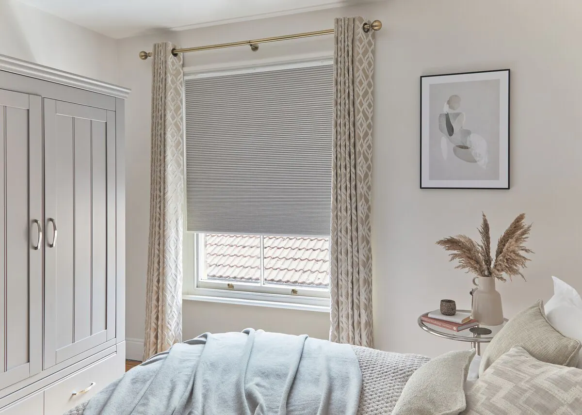 Light grey half-closed Duette® honeycomb blinds on a window in a light bedroom