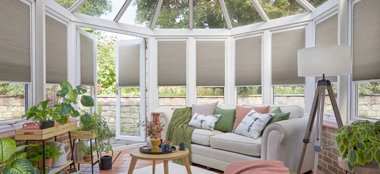 Beige Duette® honeycomb blinds on gable‑end windows in a modern conservatory‑style living room 
