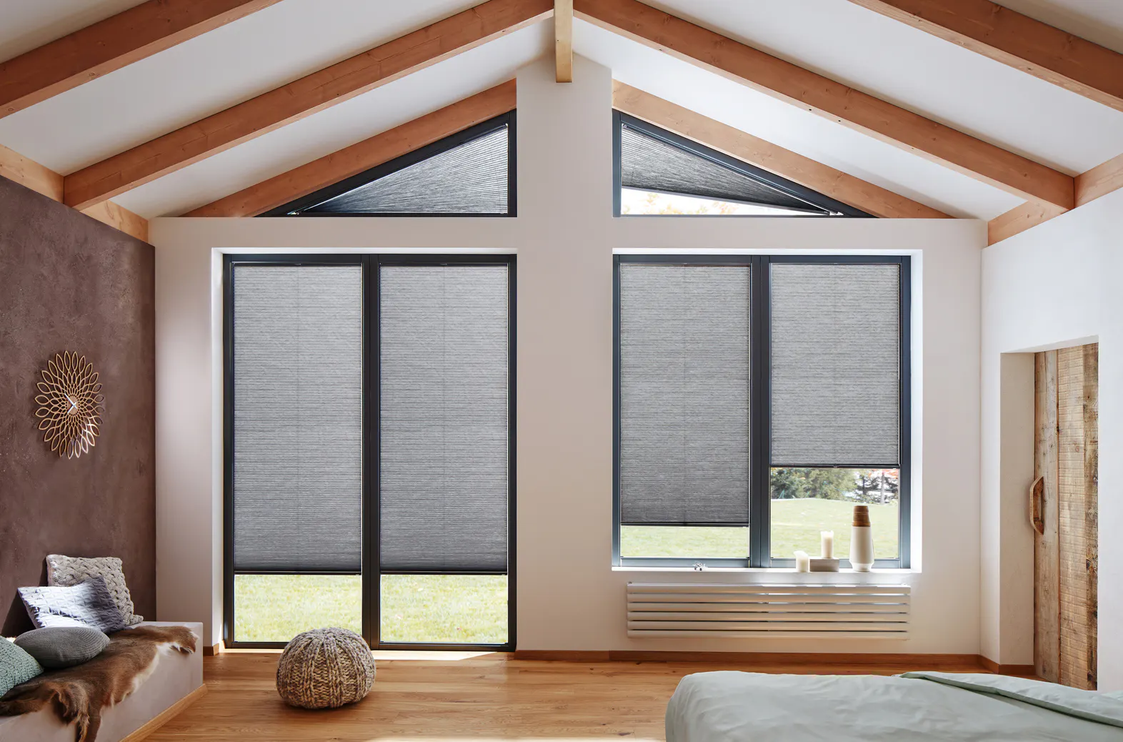 Grey Duette® honeycomb blinds on large gable‑end windows in a bright modern bedroom with wooden beams.