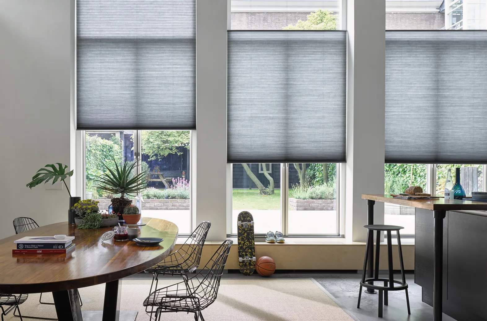 Dark grey Duette® honeycomb blinds on tall windows in a bright dining and living space.