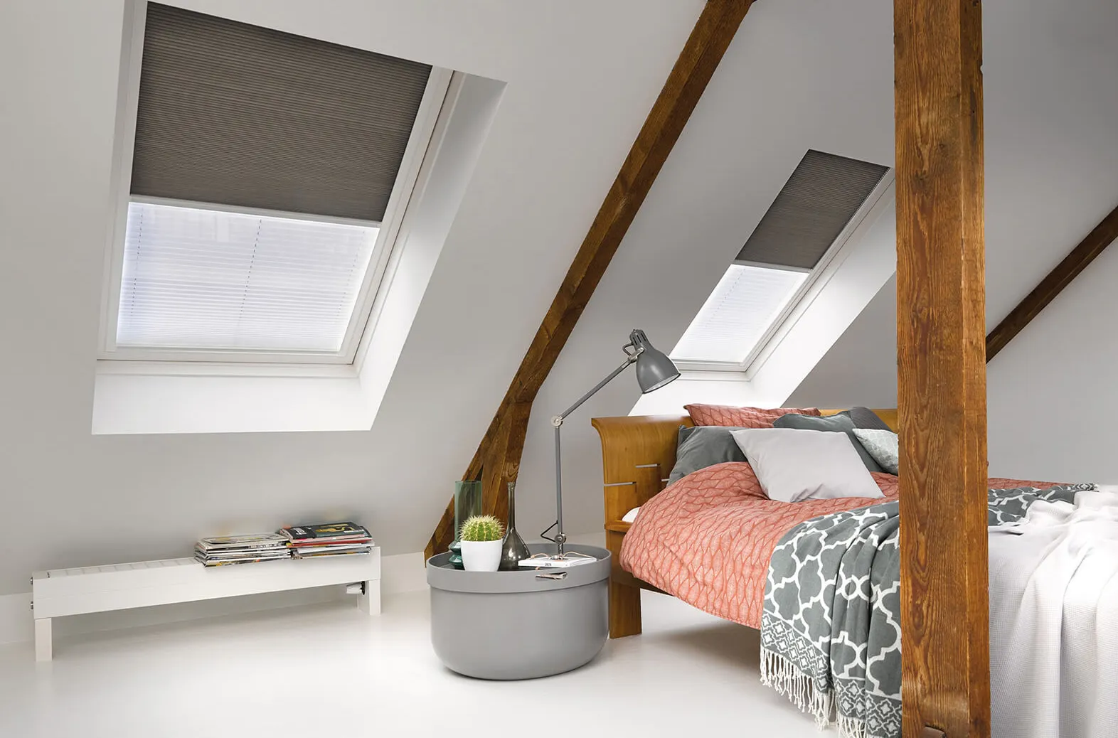 Grey Duette® honeycomb blinds on two roof windows above a cosy bedroom with wooden beams.