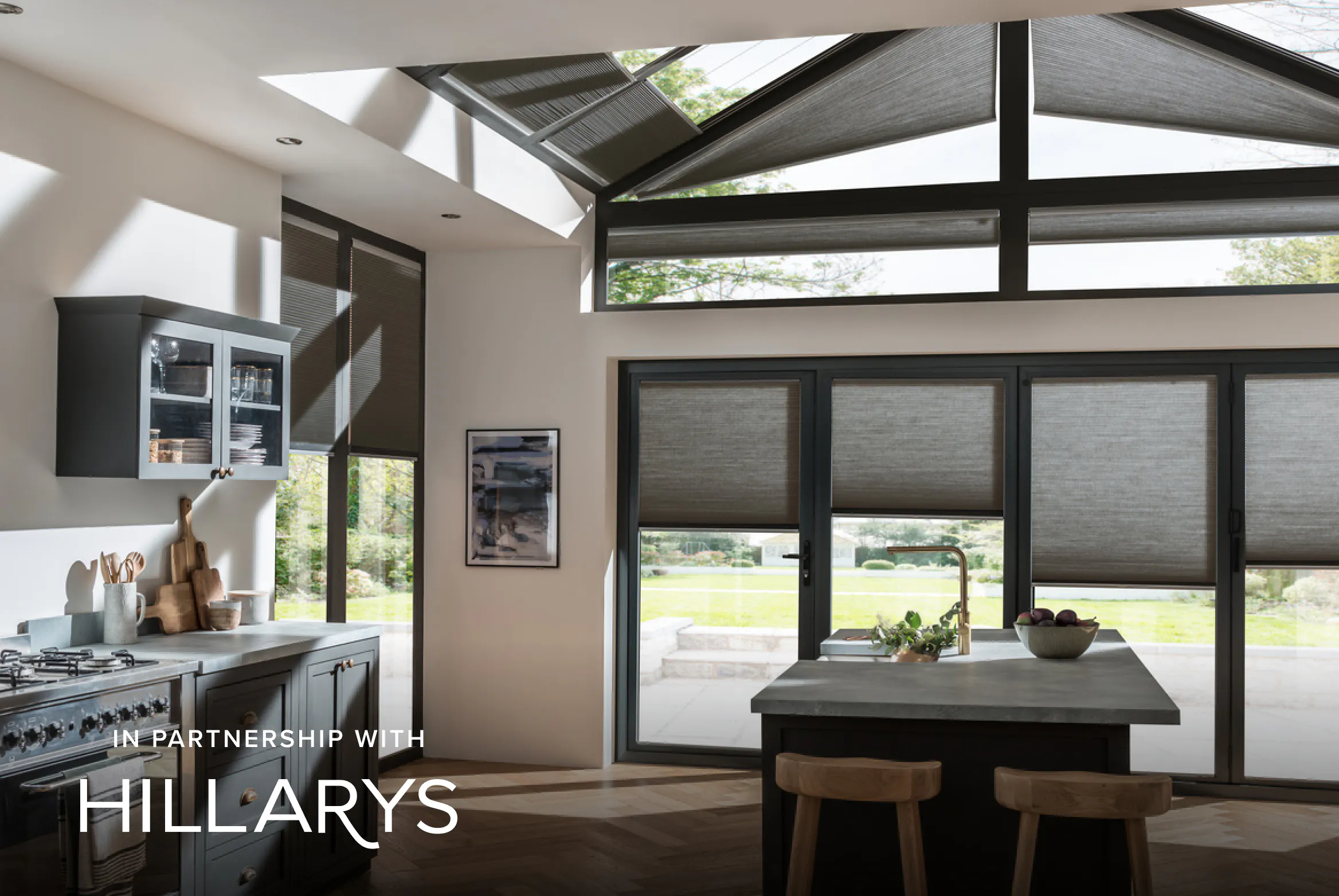 Grey Duette® honeycomb blinds on gable‑end windows in a cosy conservatory‑style kitchen.