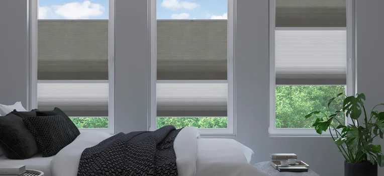 Dark grey Duette honeycomb blinds on three bedroom windows above a neatly made bed with dark patterned bedding.