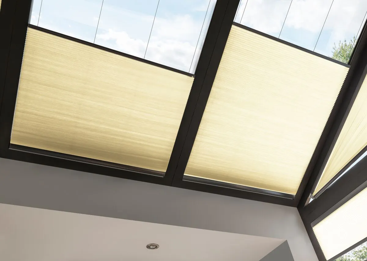 Cream Duette honeycomb blinds on large roof windows in a bright modern room with glass panels.