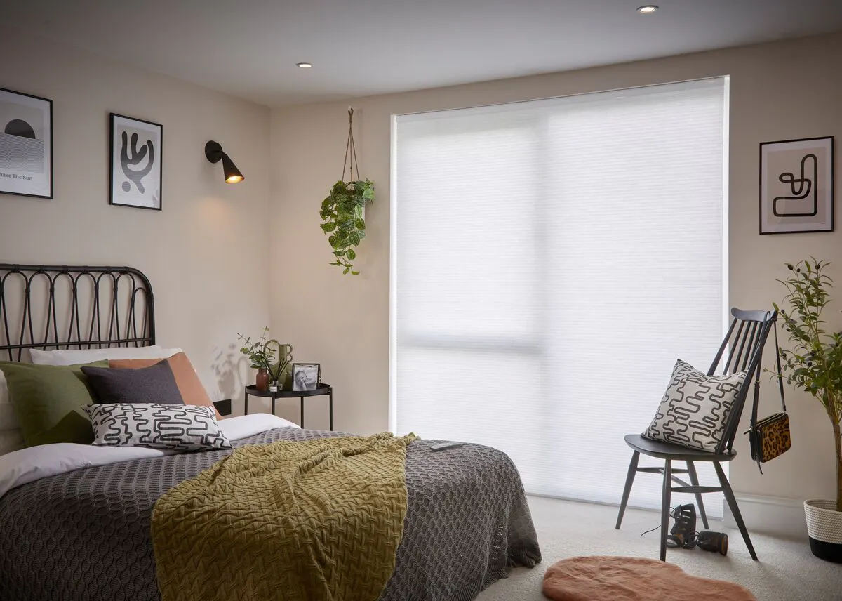 White Duette honeycomb blind on a large bedroom window behind a neatly styled room with modern décor and hanging plants.