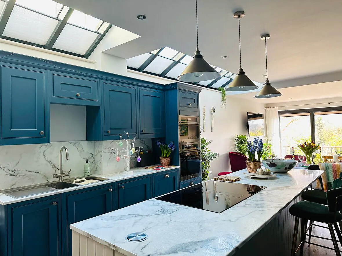 White Duette honeycomb blinds on kitchen roof windows above blue cabinets and a marble island.