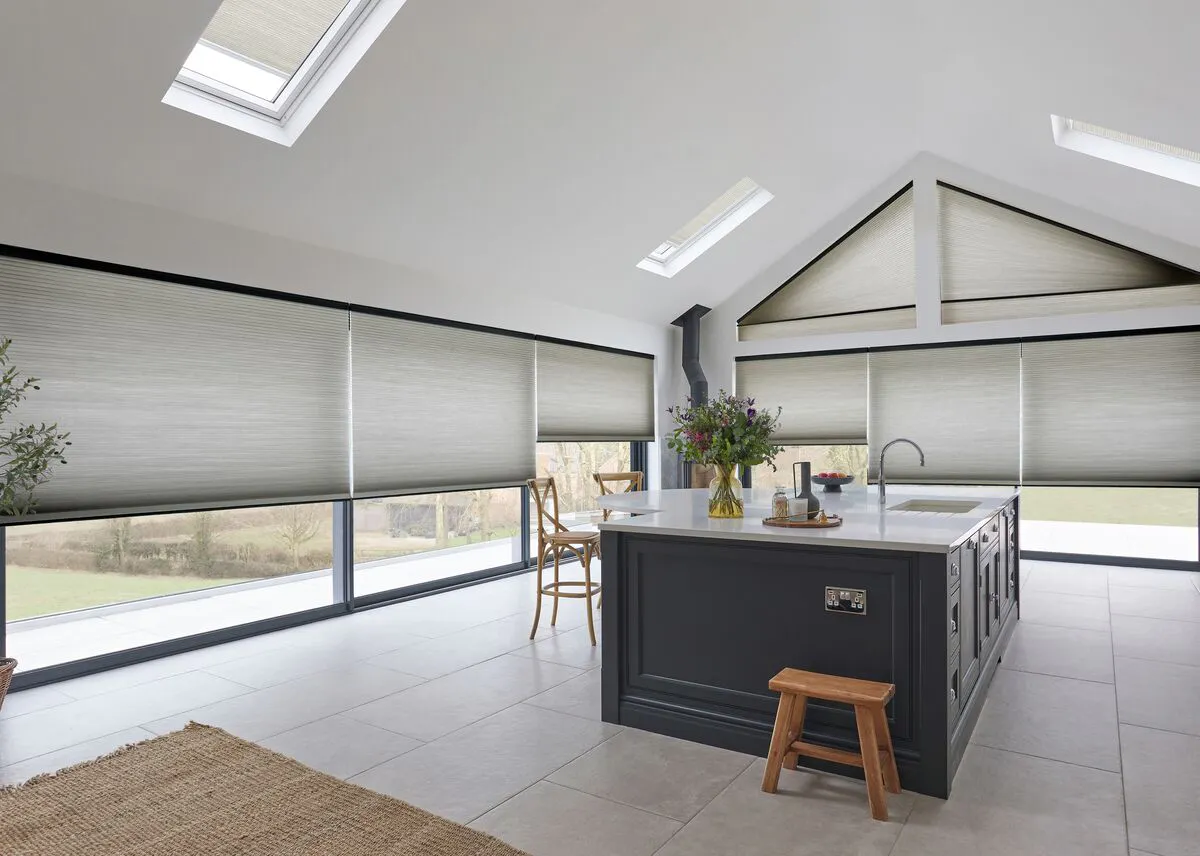Beige Duette honeycomb blinds on large kitchen windows in a modern open‑plan room with an island.