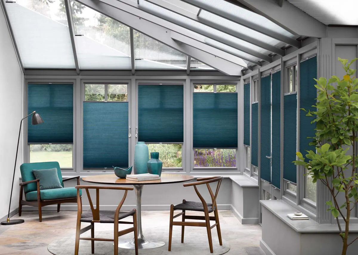 Teal Duette honeycomb blinds on conservatory roof and windows in a modern space with a dining table and chairs.