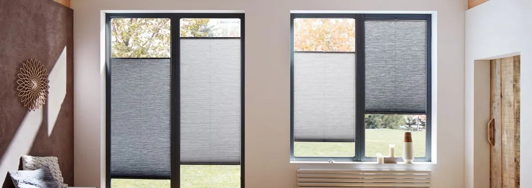 Grey Duette honeycomb blinds on tall modern windows in a bright room with soft furnishings and decorative accents.