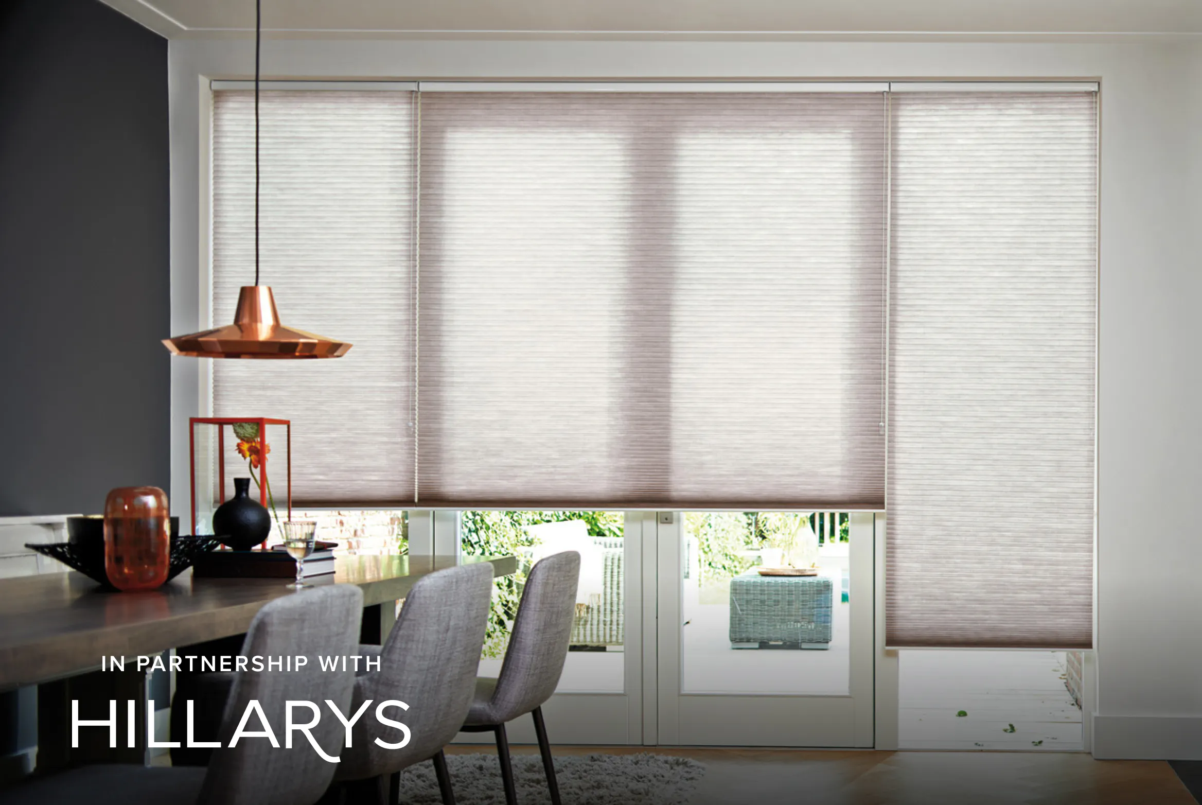Wide bi-fold doors fitted with soft beige Duette® blinds, diffusing natural light and opening the dining space onto the garden.