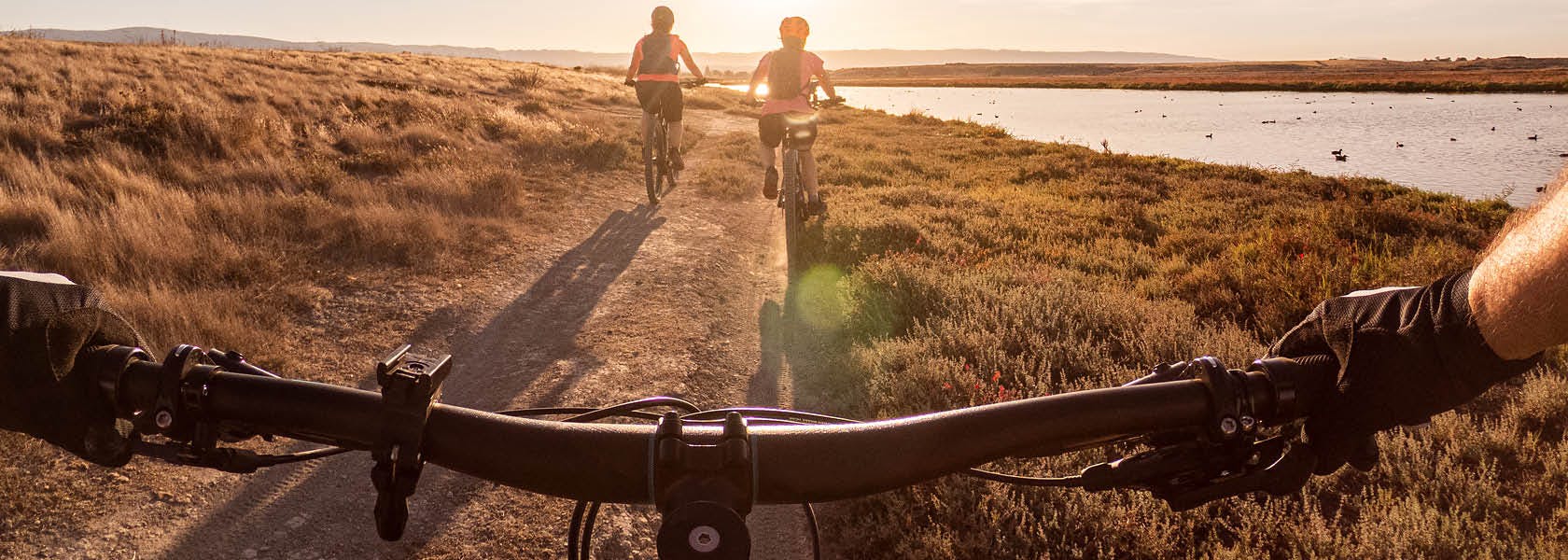 POV shot of cyclists handlebars on a path at sunset with two cyclists in front