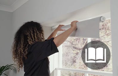 Lady hanging a white roller blind in a white room