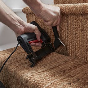 A person pushing carpet into the nook of a stair corner